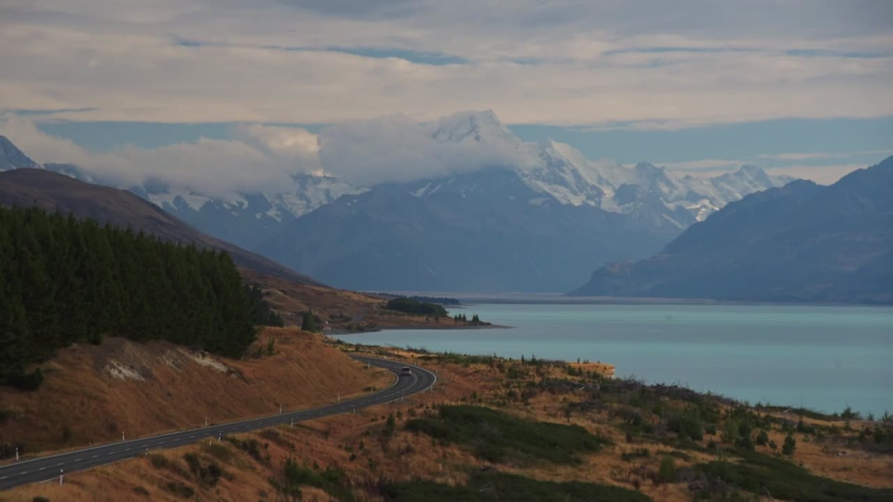 Auto che guidano lungo la costa del lago glaciale Pukaki, verso le Alpi Meridionali e il Monte Cook nell'Isola del Sud della Nuova Zelanda.