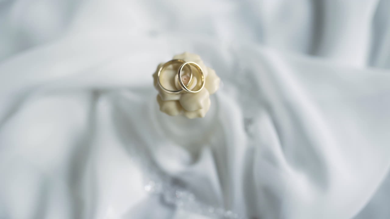 Elegante goldene Eheringe, ineinander verschlungen auf weichem weißem Stoff.