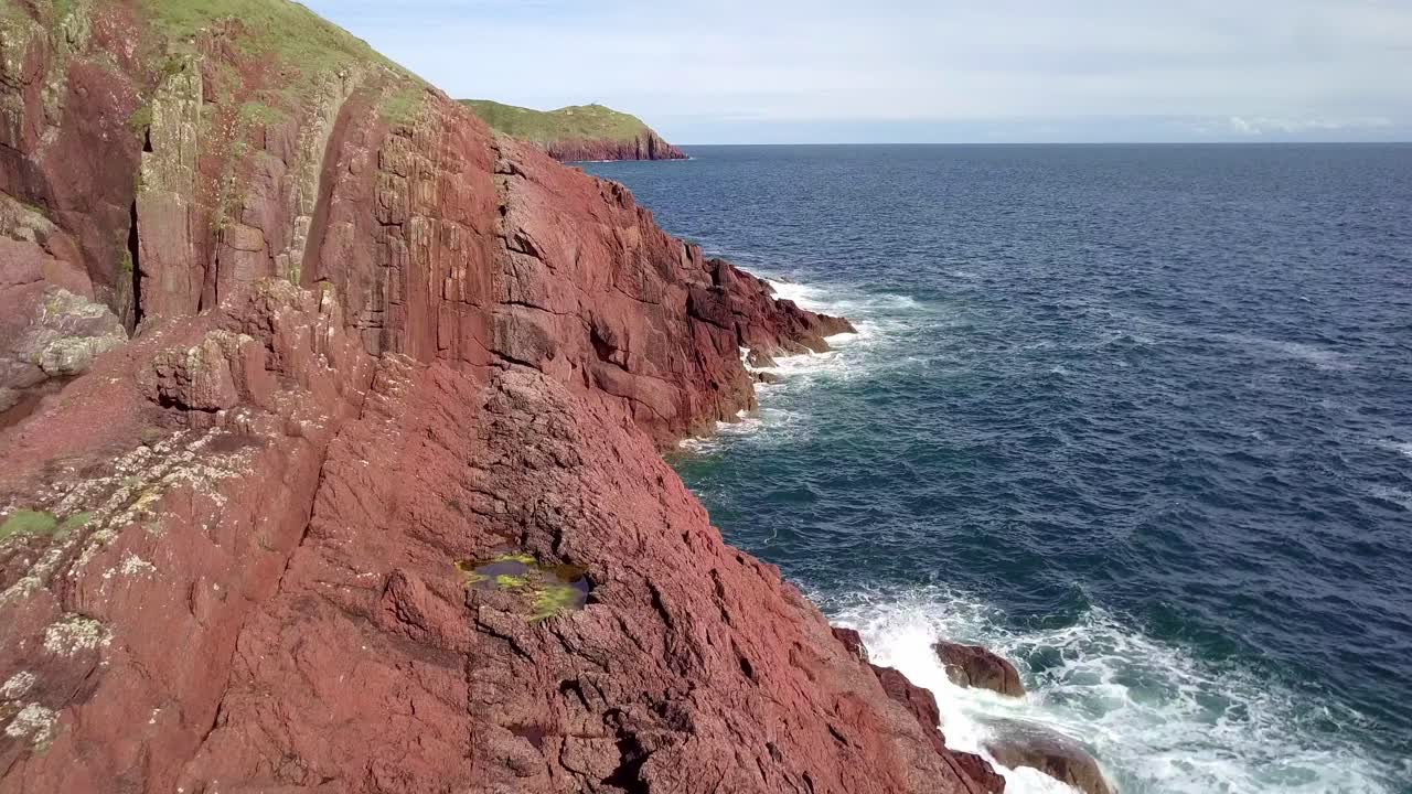 푸른 하늘과 부서지는 파도가 있는 붉은 웨일스 절벽의 드론 아리엘 영상