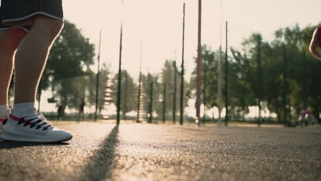 Nahaufnahme-Der-Beine-Von-Sportlern,-Die-Bei-Sonnenuntergang-Auf-Einem-Basketballplatz-Im-Freien-Den-Ball-Treten-Und-Einander-Zuspielen