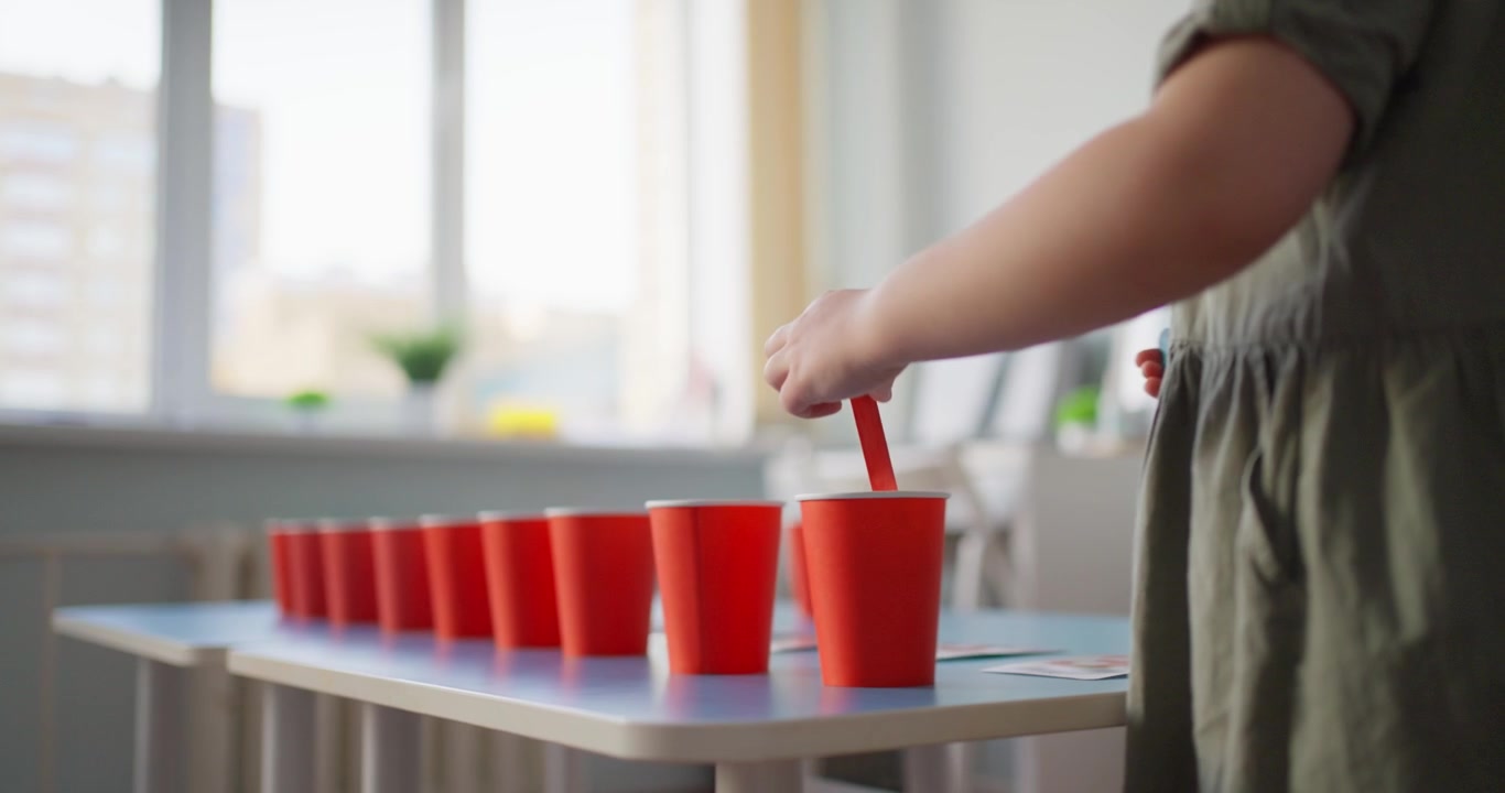 Bambina che gioca a un gioco educativo di smistamento con bicchieri rossi e bastoncini colorati