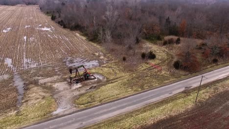 Toma-Aérea,-Moviéndose-De-Derecha-A-Izquierda,-De-Un-Gato-De-Bomba-De-Campo-Petrolífero-Que-Opera-En-Un-Campo-Abierto-Junto-A-Una-Carretera-Rural