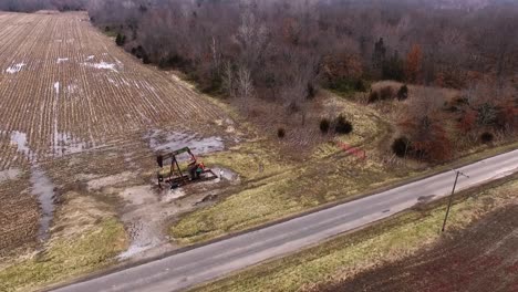 toma aérea, moviéndose de derecha a izquierda, de un gato de bomba de campo petrolífero que opera en un campo abierto junto a una carretera rural