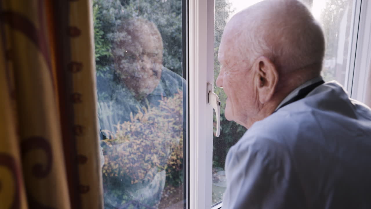 Elderly man looking out window with reflection