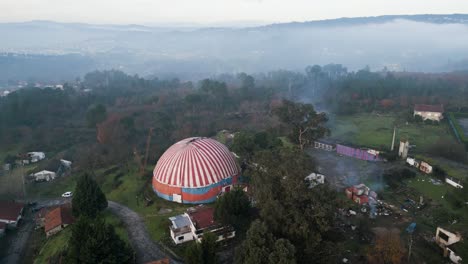 drone rises above benposta circus tent with mist on treetop canopy