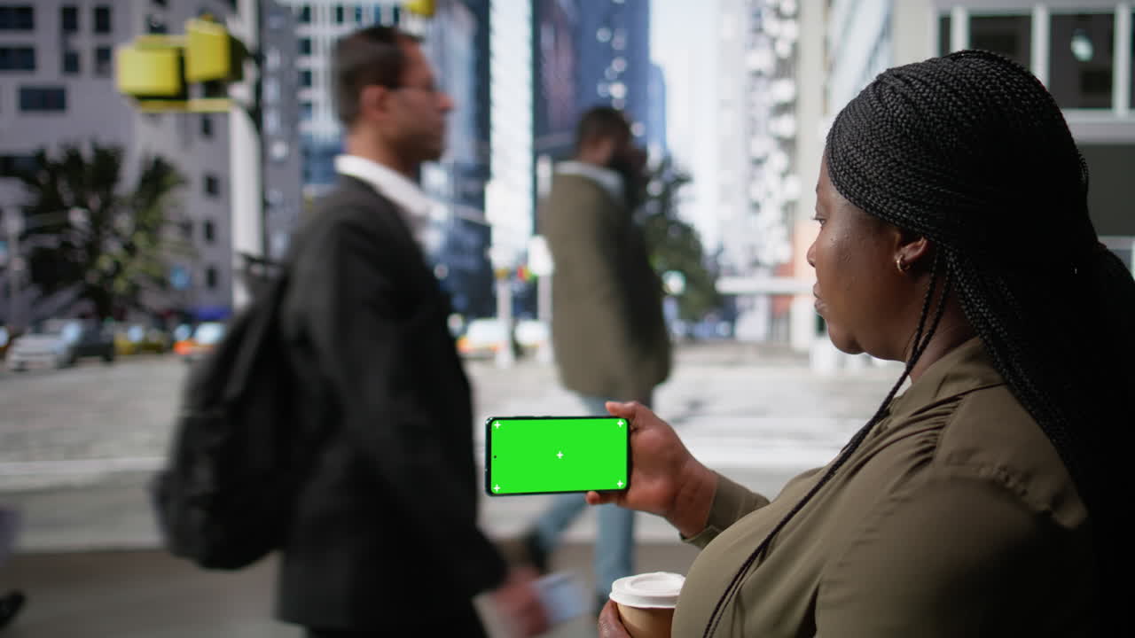 Horizontal green screen on phone held by black woman near city movement