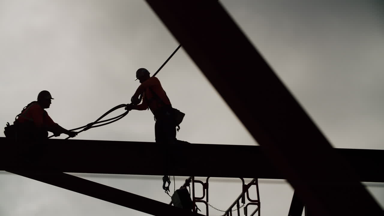 Silhouetted construction workers on a steel beam against a cloudy sky