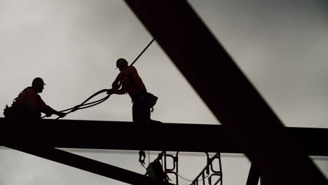 silhouetted construction workers on a steel beam against a cloudy sky