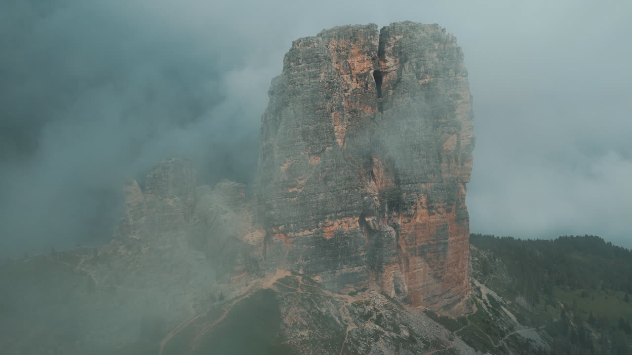 Misty clouds swirling around rugged rocky peaks of Cinque Torri, enveloping dramatic mountain landscape in Italian Dolomites with ethereal atmospheric conditions