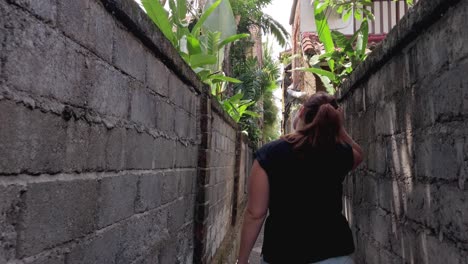 White-caucasian-woman-walking-through-a-narrow-alley-in-the-tropical-city-of-Ubud,-Bali-exploring-the-area,-tourist