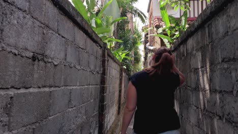 white caucasian woman walking through a narrow alley in the tropical city of ubud, bali exploring the area, tourist