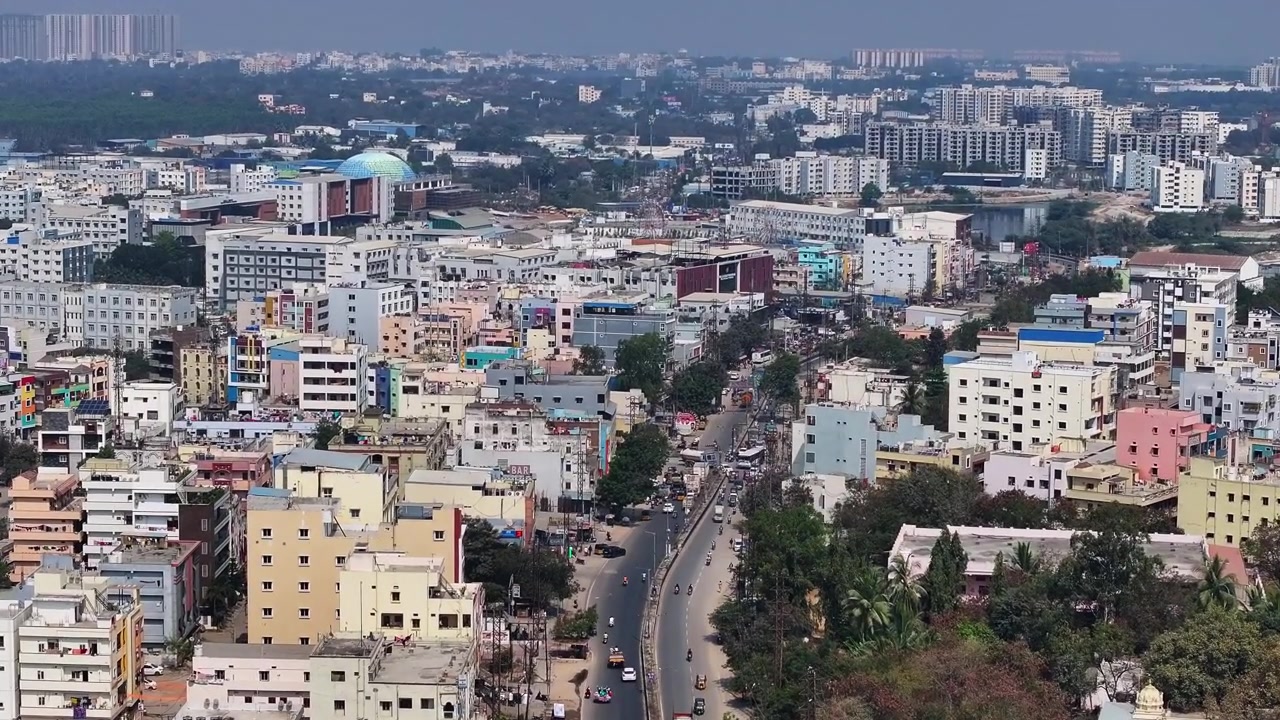 Edifici residenziali con appartamenti, ospedali, college, lago e traffico leggero sulla strada Medak a Suraram, Quthbullapur, Hyderabad, Telangana, India. Di giorno, ripresa con avvicinamento, ripresa con drone, 4K.