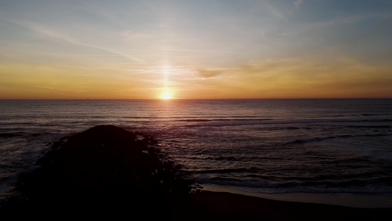 waves glisten beneath warm sunset behind rocky jetty into sea