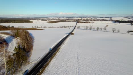 Luftdrohne,-Die-An-Einem-Sonnigen-Tag-Mit-Blauem-Himmel-über-Die-Winterschneelandschaft-über-Autos-Auf-Einer-Landstraße-In-Richtung-Der-Fernen-Stadt-Zvitavy-In-Der-Tschechischen-Republik-Schwenkt