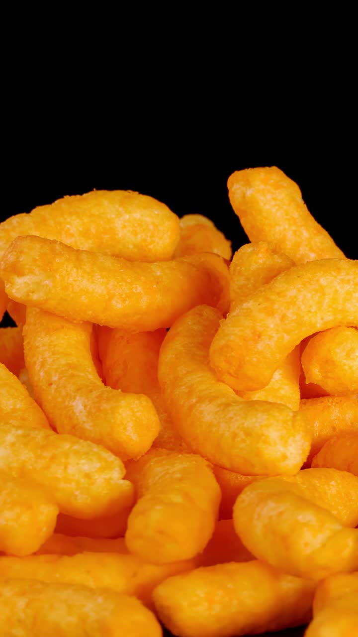 Soffietti al formaggio croccanti ruotano in macro, con illuminazione vivace, sfondo nero e texture dettagliata.