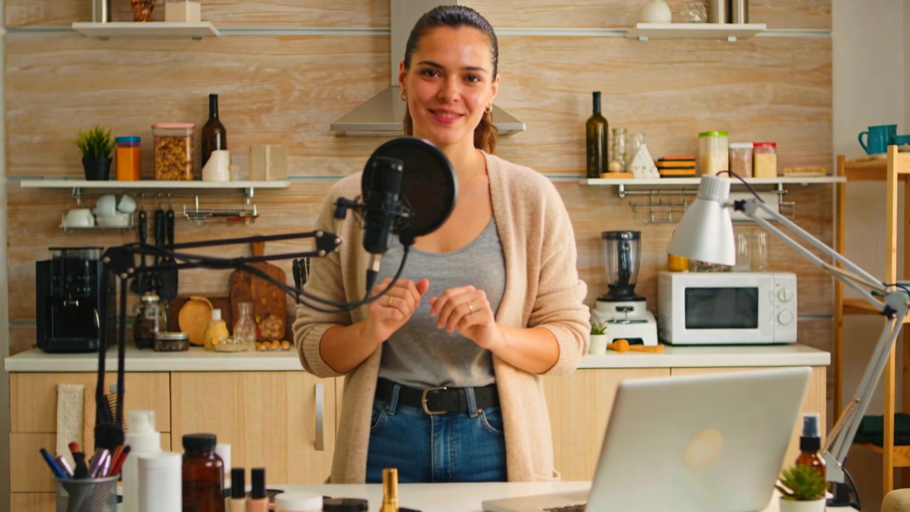 Inizio della registrazione, una presentatrice in cardigan presenta cosmetici in cucina, usando un microfono.