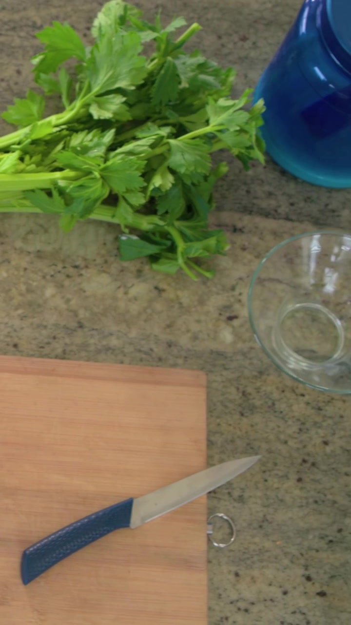 Video verticale: Spostando un mazzo di sedano mentre una brocca e una ciotola vengono posizionate sul bancone, per la preparazione.