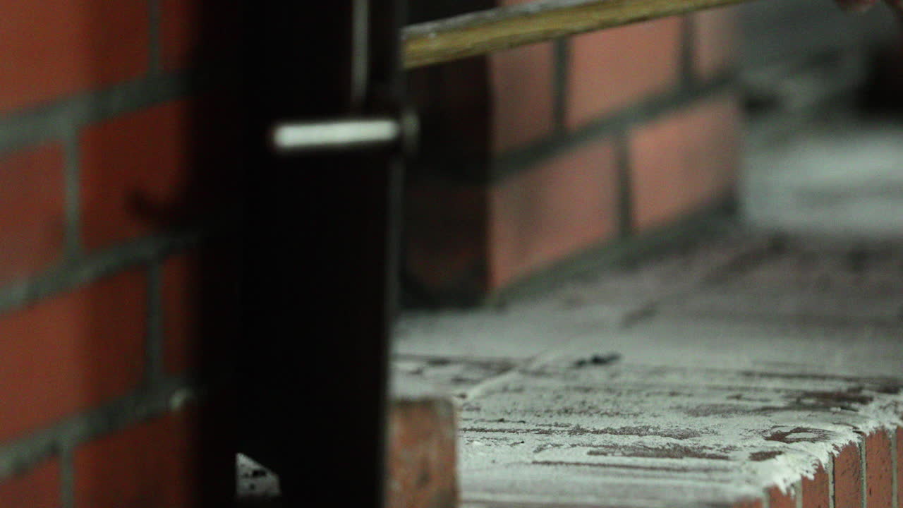 베이커는 사워도우 반죽을 얇은 금속 껍질에 올려 베이커리의 전통적인 벽돌 오븐에 넣습니다.