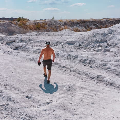 strong man in white canyon. healthy man without shirt walking on a rocky background in summer. aerial view on a sporty male in cap and shorts in nature.