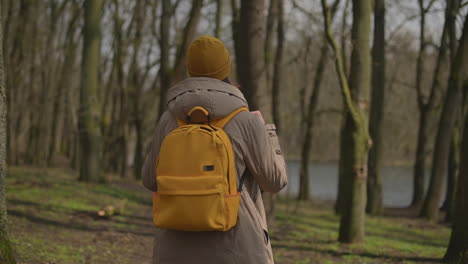 una joven con una gorra de lana amarilla y una mochila amarilla camina por el bosque mirando de un lado a otro