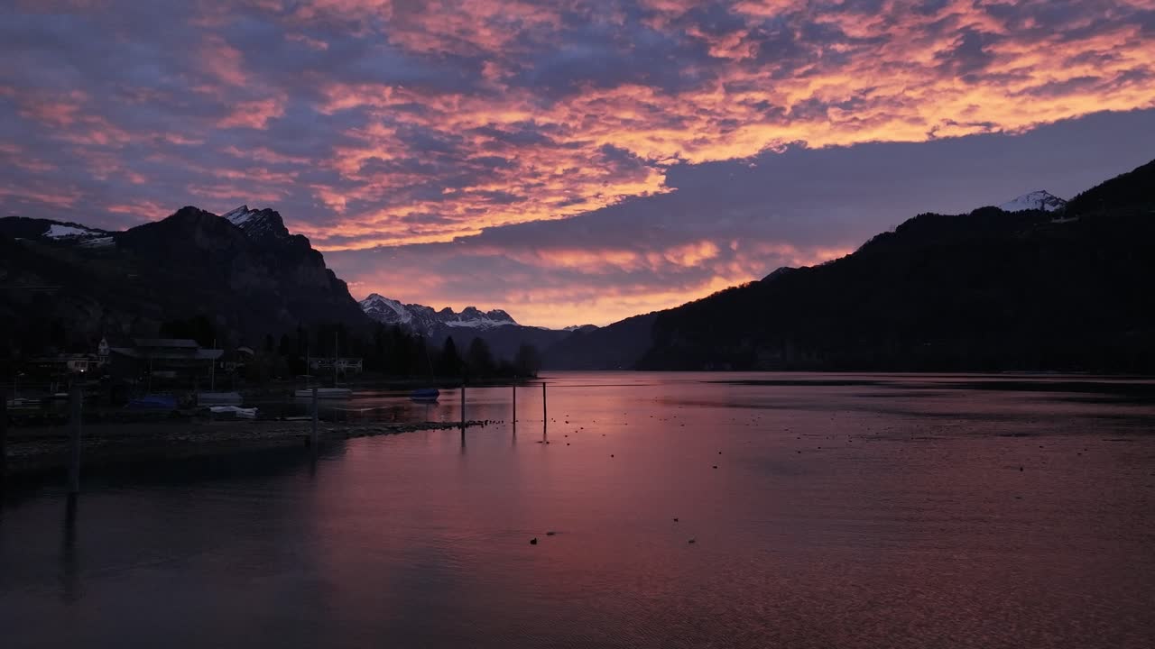 Sunset over the Walensee in Switzerland. The sky is ablaze with vibrant hues of orange and purple, reflecting on the calm waters of the lake.