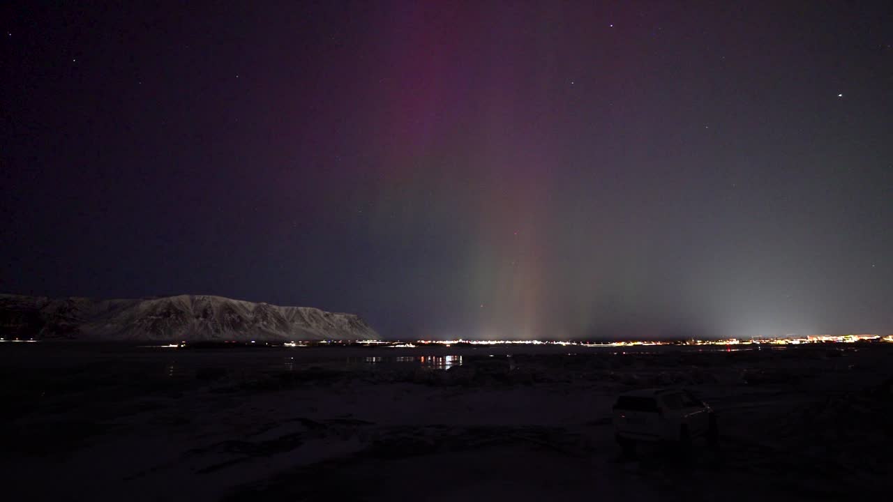 Time lapse wide shot of aurora borealis with Purple sky at night. Snowy mountains and driving cars on road.