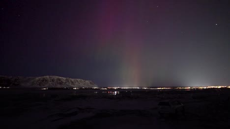 time lapse wide shot of aurora borealis with purple sky at night. snowy mountains and driving cars on road.