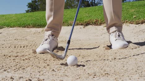 low section of caucasian senior man hitting golf ball out of a sand trap at golf course on a bright