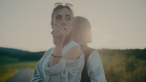 thoughtful female friends standing back to back against sky