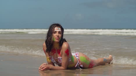 The-sunlit-shores-of-the-Caribbean-hosted-a-captivating-scene-with-a-young-girl-in-a-bikini,-her-body-painted-in-lively-colors-laying-in-the-waves-of-the-ocean