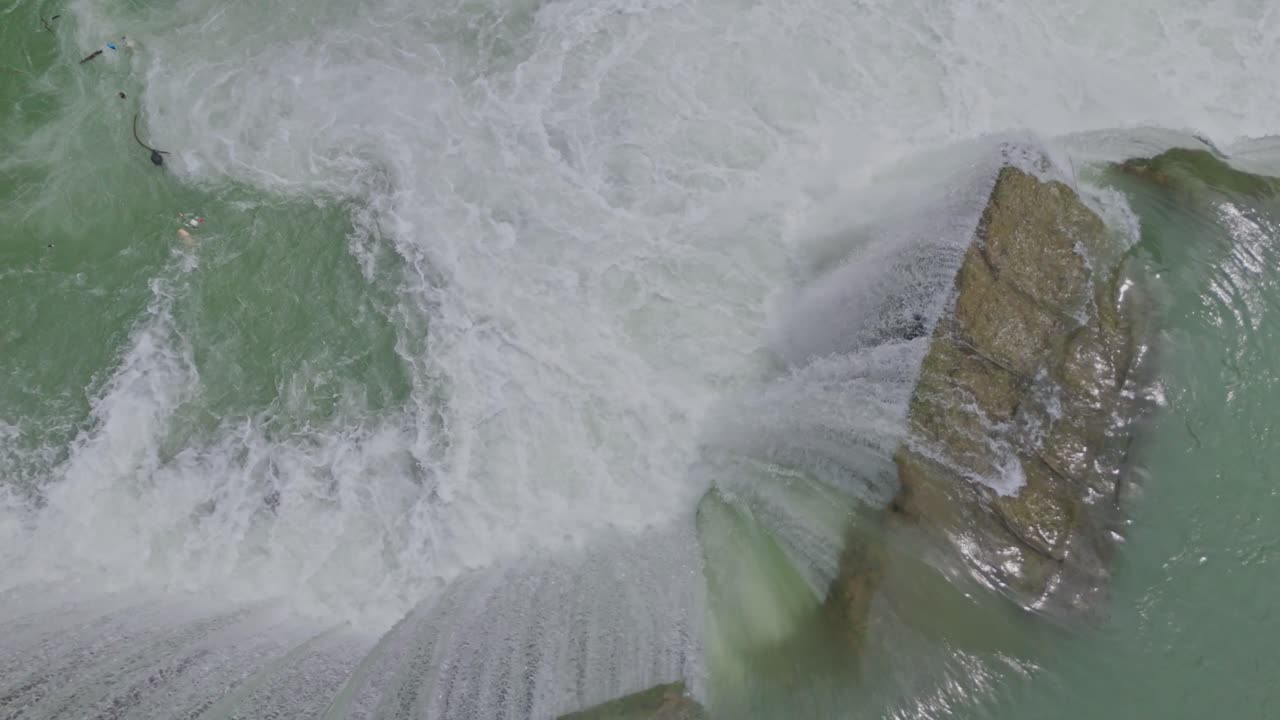 Aerial drone view of a beautiful waterfall merging into a flowing river, capturing the natural beauty of water movement, rocky terrain, and pristine landscape
