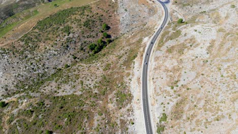 Drone-shot-tilting-up-and-moving-forward,-filming-some-cars-driving-on-a-road-in-the-hills-in-Andalusia,-Spain