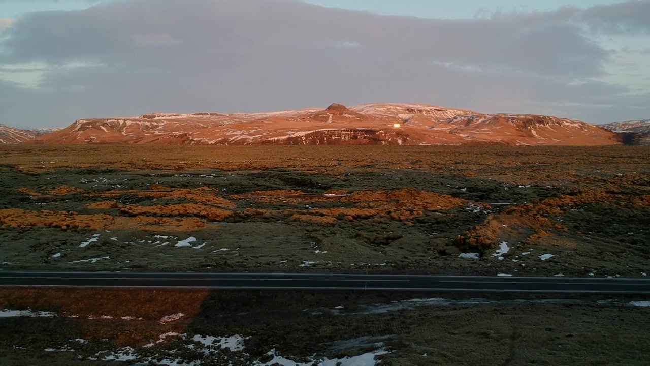 Vista aérea de drone da paisagem típica da Islândia com uma estrada no meio, areia vermelha, montanhas vermelhas, solo verde e neve