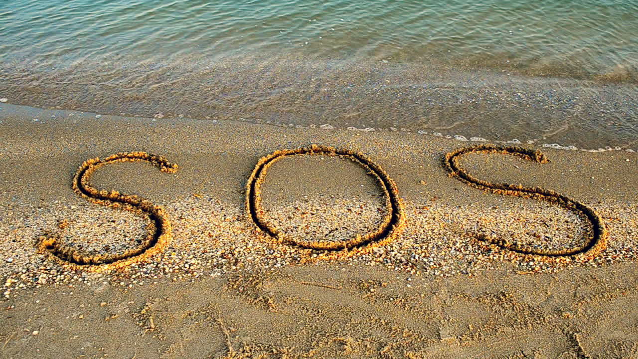 Inskriptionen SOS i sanden. Filmning på stranden