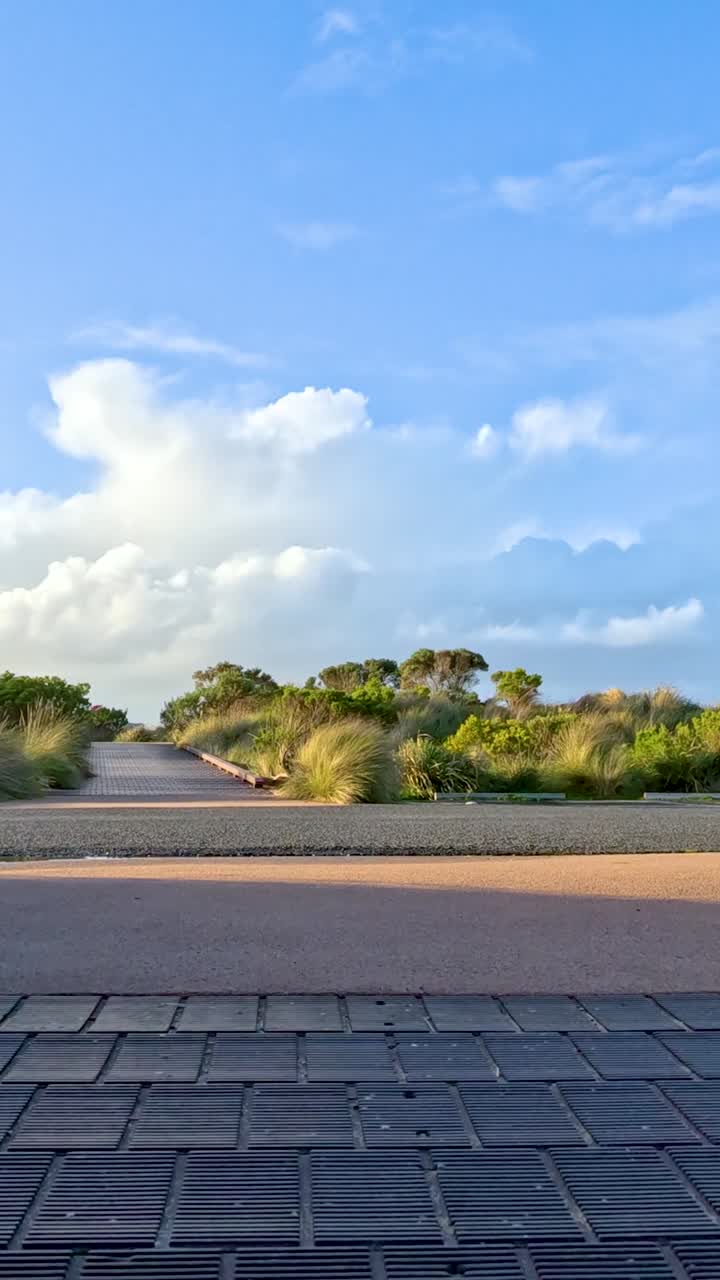 Jalan-jalan santai di sepanjang jalan setapak bata dikelilingi tanaman hijau subur dan langit terbuka di Great Ocean Road