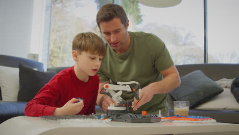 Father-and-son-wearing-pyjamas-building-robotic-arm-from-plastic-kit-at-home-for-science-project---shot-in-slow-motion