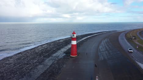 drone shot of a lighthouse by the dutch coastline, with a guy standing next to it, flying to the left and panning right.