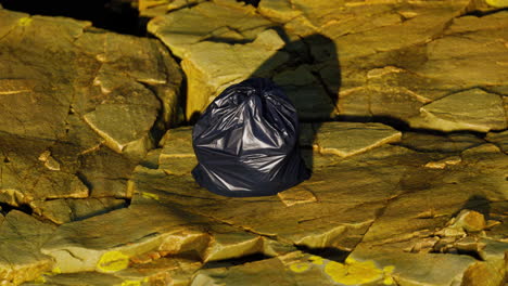 black trash bag lay on a rocky beach