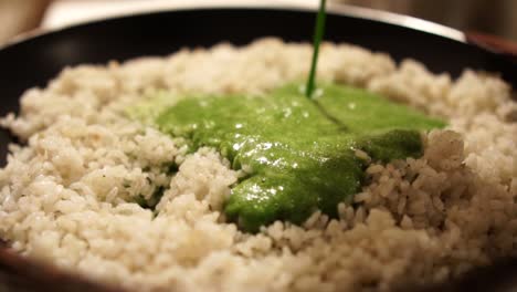 pouring green spinach puree into a pan full of cooked rice, slow motion