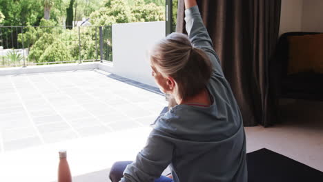 senior woman practicing yoga at home, stretching with water bottle nearby, copy space