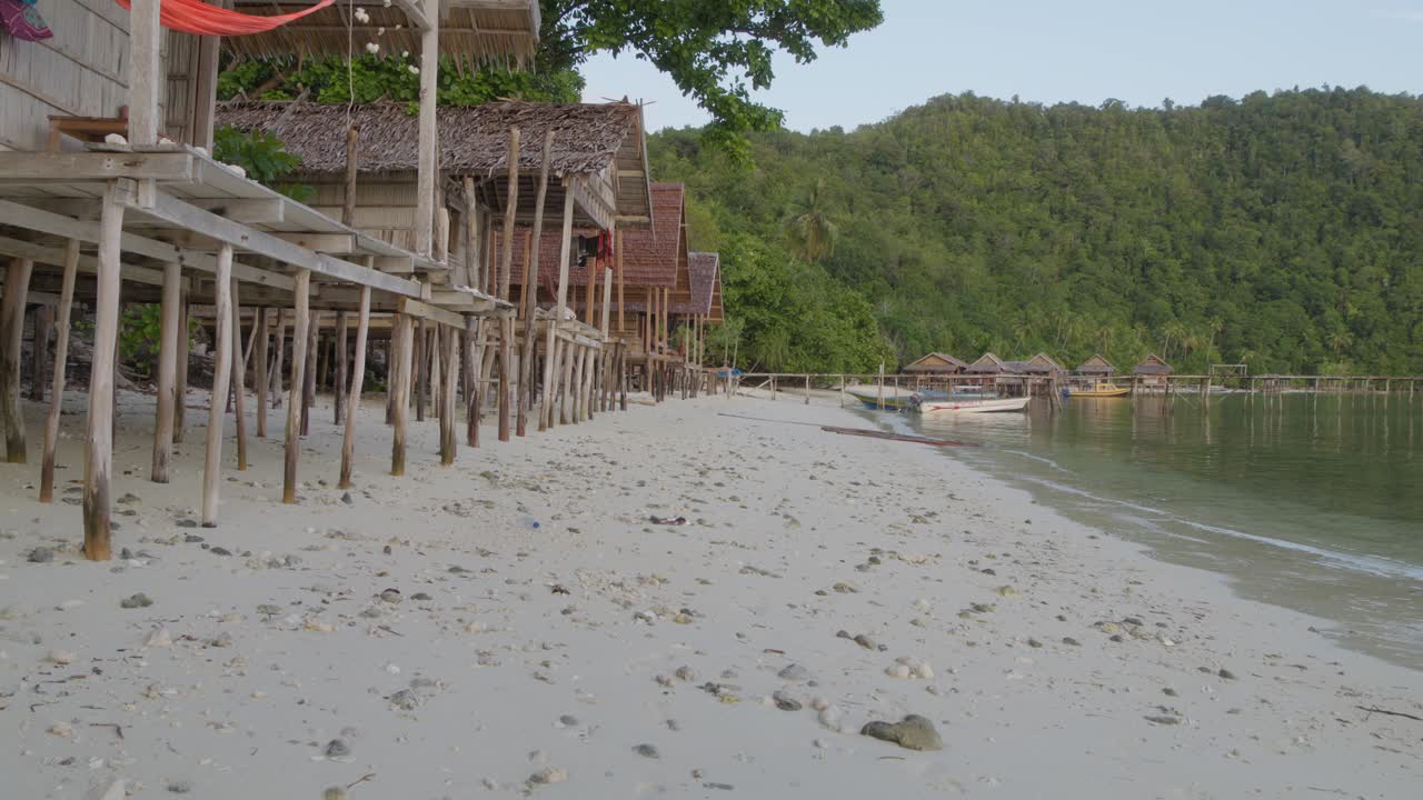 cabañas de madera en la playa de arena de la isla de kri en el archipiélago de raja ampat de indonesia, arruinadas por la desafortunada vista de dos botellas de plástico ensuciando el paisaje prístino.