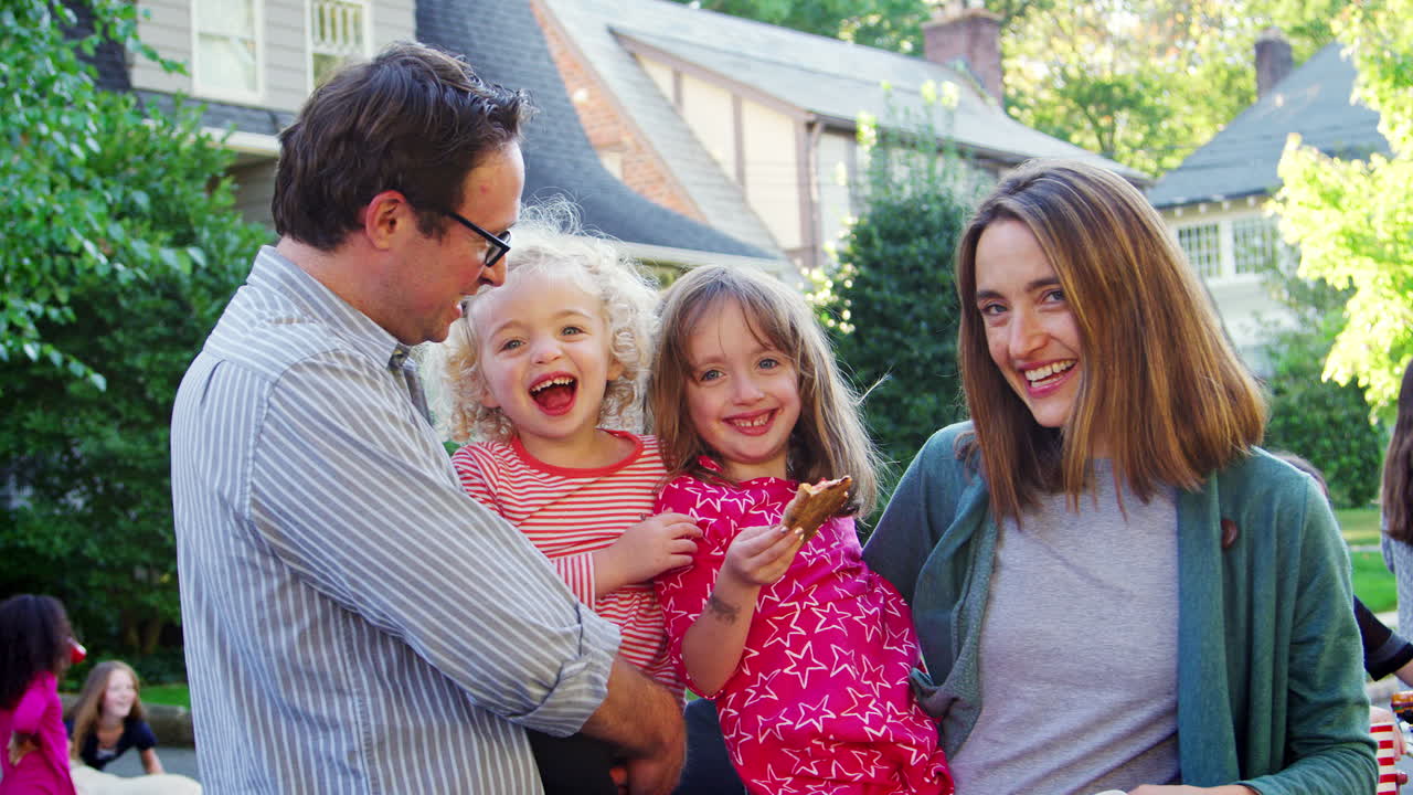 어린 아이 들 을 들고 있는 부모 들 이 블록 파티 에서 카메라 에 미소 짓고 있다