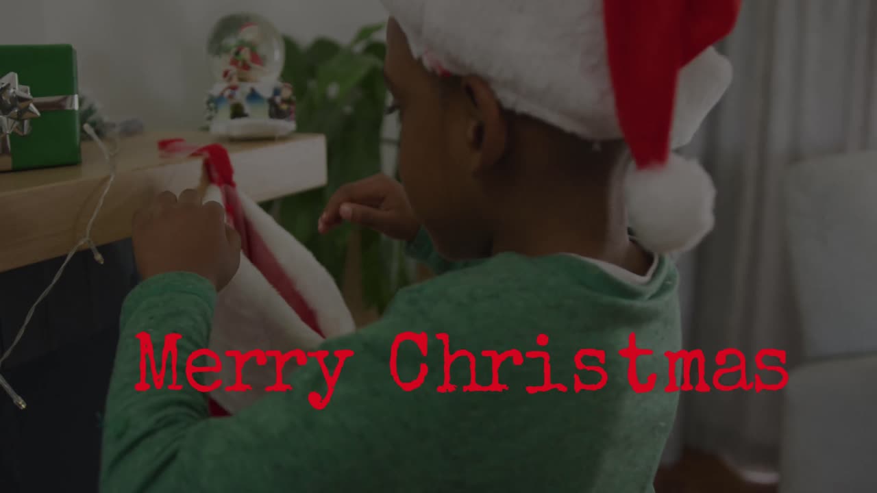 animación del texto de feliz navidad sobre un niño afroamericano que lleva el sombrero de papá noel.
