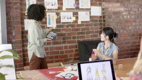 diversos diseñadores ocupados usando portátiles y discutiendo el trabajo en el estudio de diseño de moda en cámara lenta
