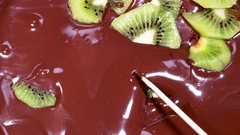 kiwi slices being mixed into melted chocolate