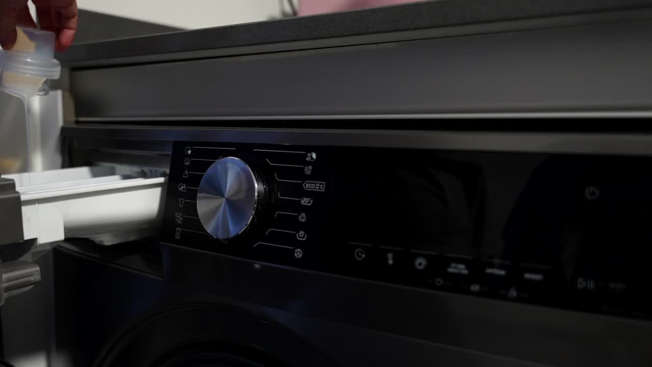 Una mano aggiunge detersivo nel cassetto della lavatrice a carica frontale, l'accende e seleziona il programma.