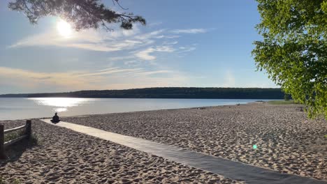 Woman-Doing-Yoga-On-Beach-During-Sunset-Panning-Across-Beach-Wide-Angle-Clouds-and-Trees