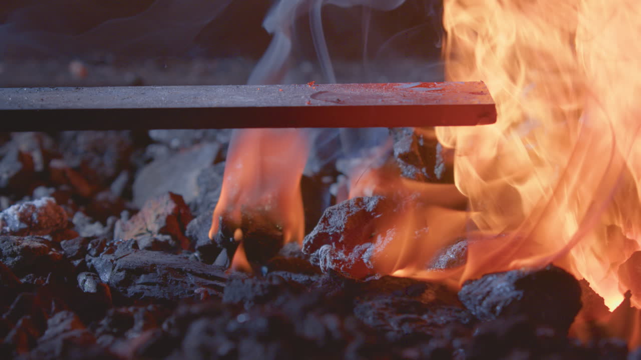 Closeup of blacksmith inserting metal piece into hot flames and coals of forge