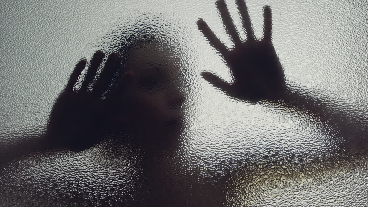 A female silhouette behind the frosted window touches the glass slowly