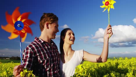 romantic couple blowing pinwheel in mustard field